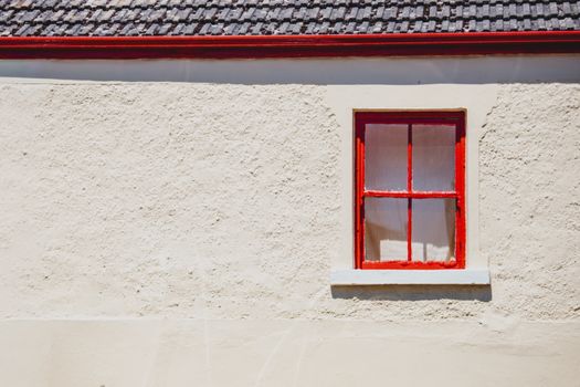 Red-framed window on a textured wall in Carlingford, Ireland, showcasing minimalist architecture.