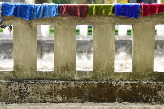 Vibrant towels hang on an aged concrete railing in an outdoor setting.