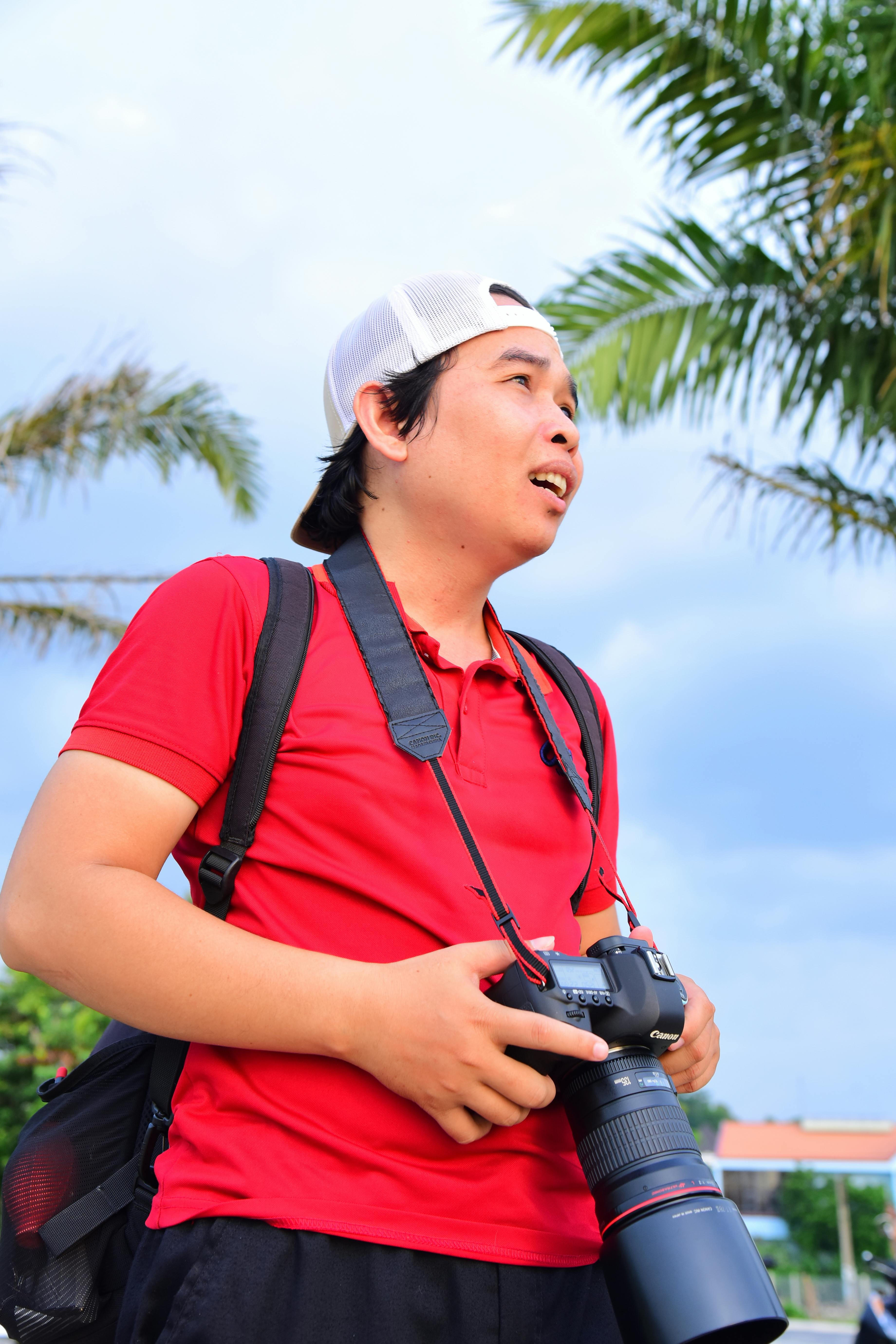 Photographer in red shirt outdoors with a camera, capturing tropical scenery.