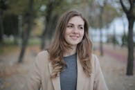 Happy millennial female in casual clothes looking away and smiling while standing against blurred trees in city park in daytime