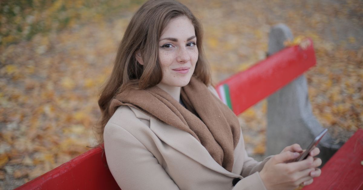 A person sitting on a park bench, looking at the sky, with no phone in hand, smiling