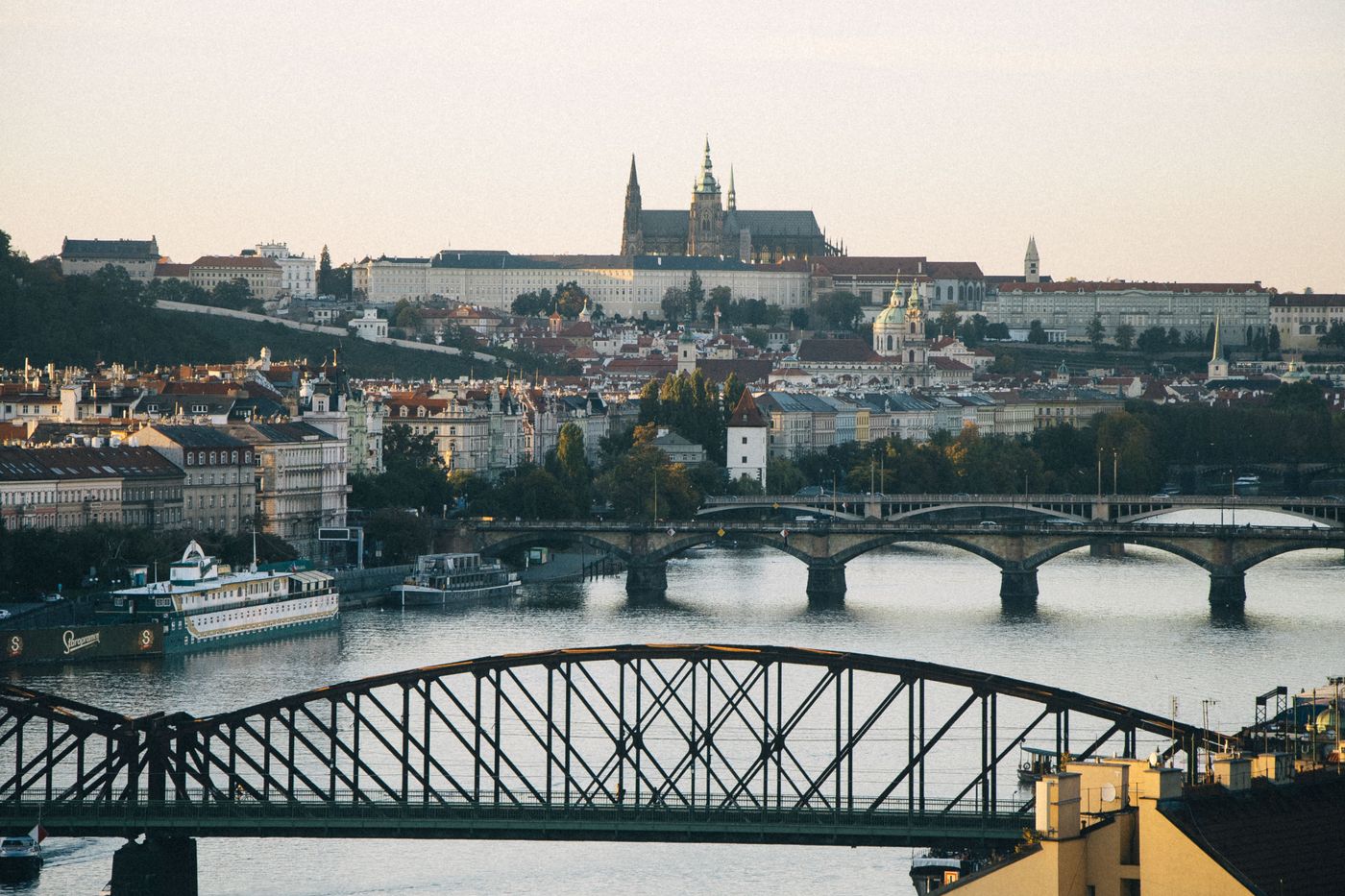 Prague's skyline at dusk with the Vltava River in the foreground and Prague Castle on the hill behind, reflected in the water.