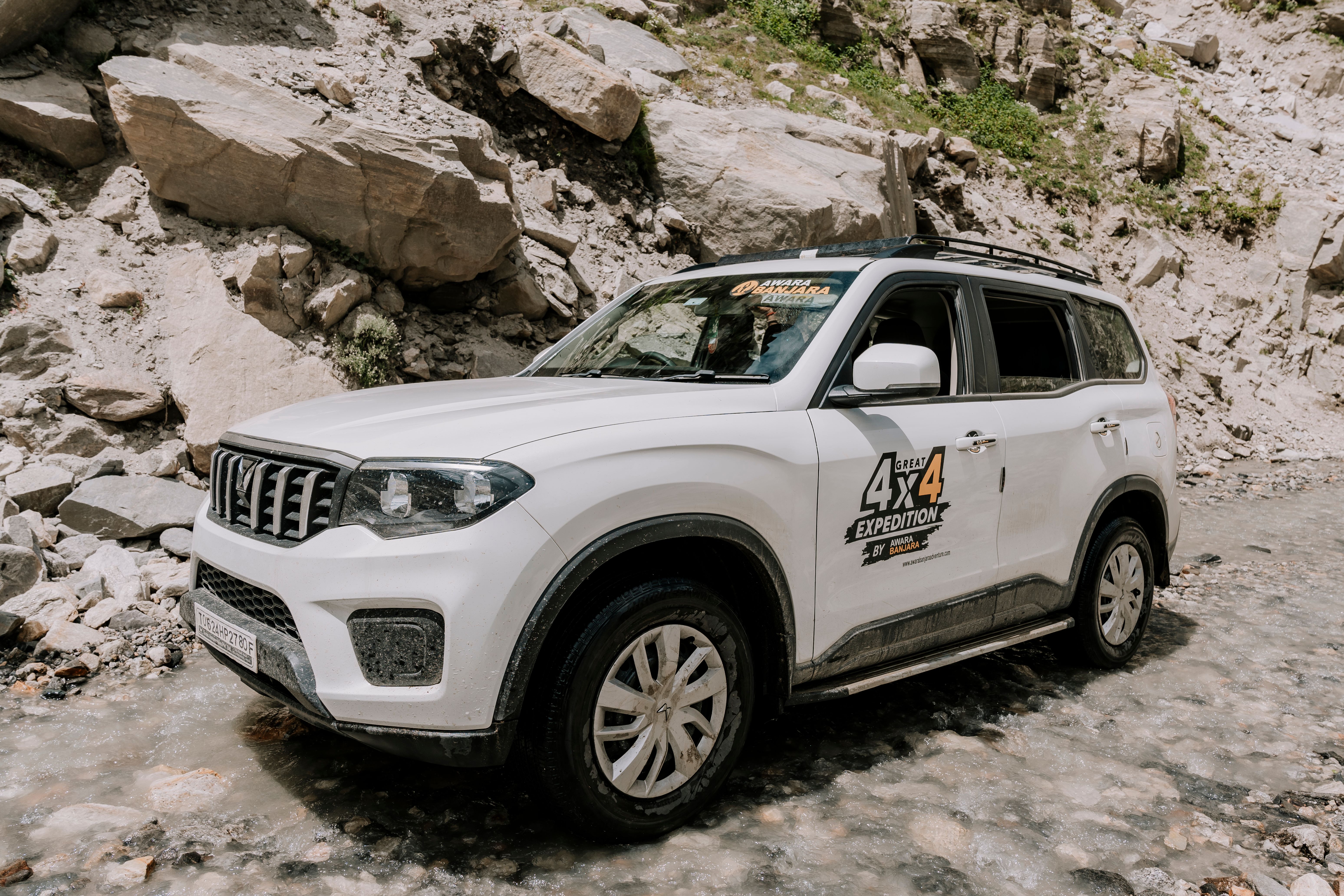 White SUV driving over rocky terrain during a summer off-road expedition.