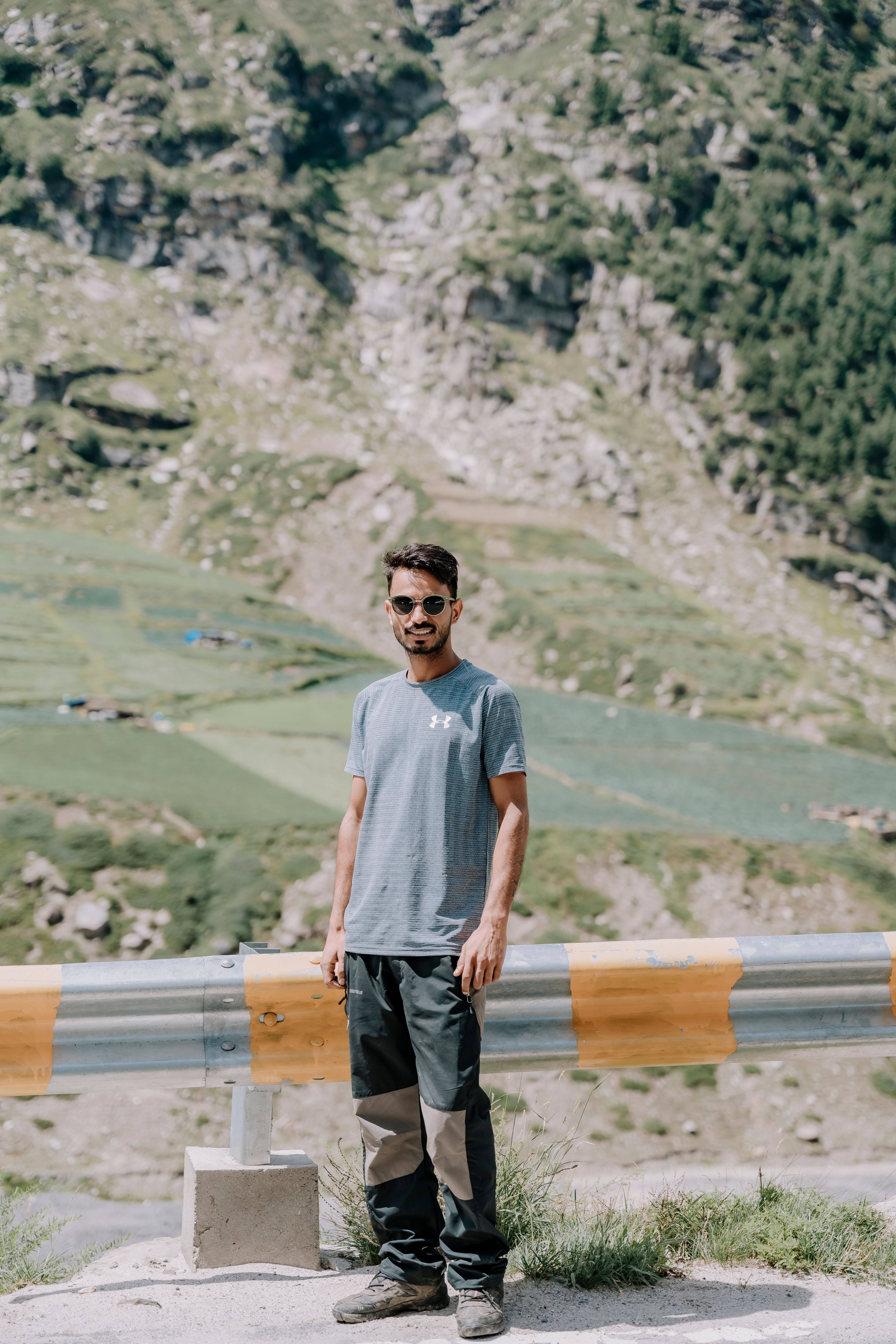 A young male adventurer stands by a guardrail, showcasing a scenic mountain view.