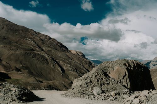 Free Dramatic rocky mountain landscape with a dirt road under a vibrant blue sky and scattered clouds. Stock Photo