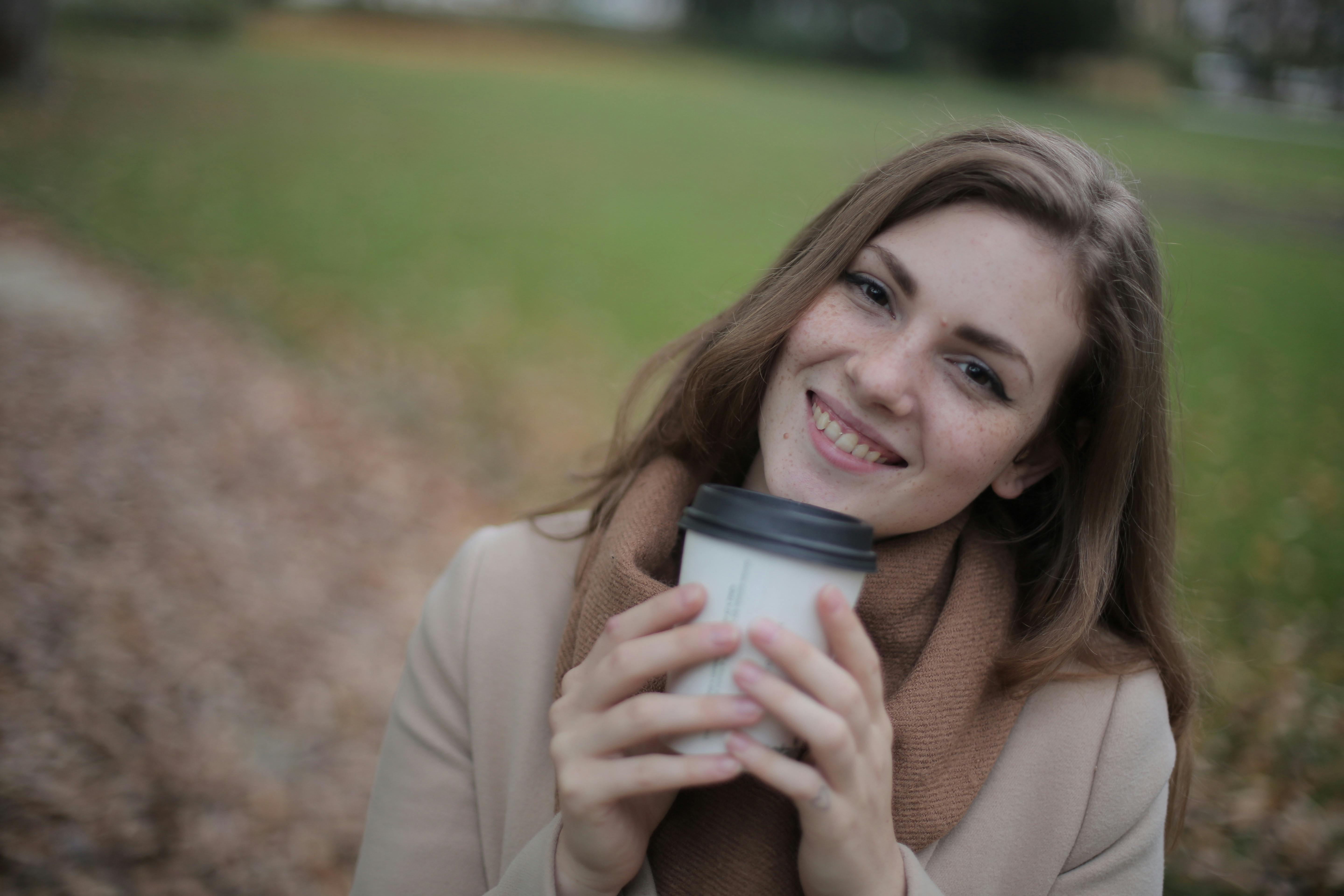 一位穿着棕色外套的女人在公园里拿着咖啡杯微笑