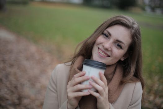 一位穿着棕色外套的女人在公园里拿着咖啡杯微笑