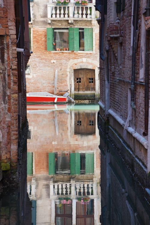 Free A tranquil Venice canal reflecting historic architecture with a boat docked nearby. Stock Photo