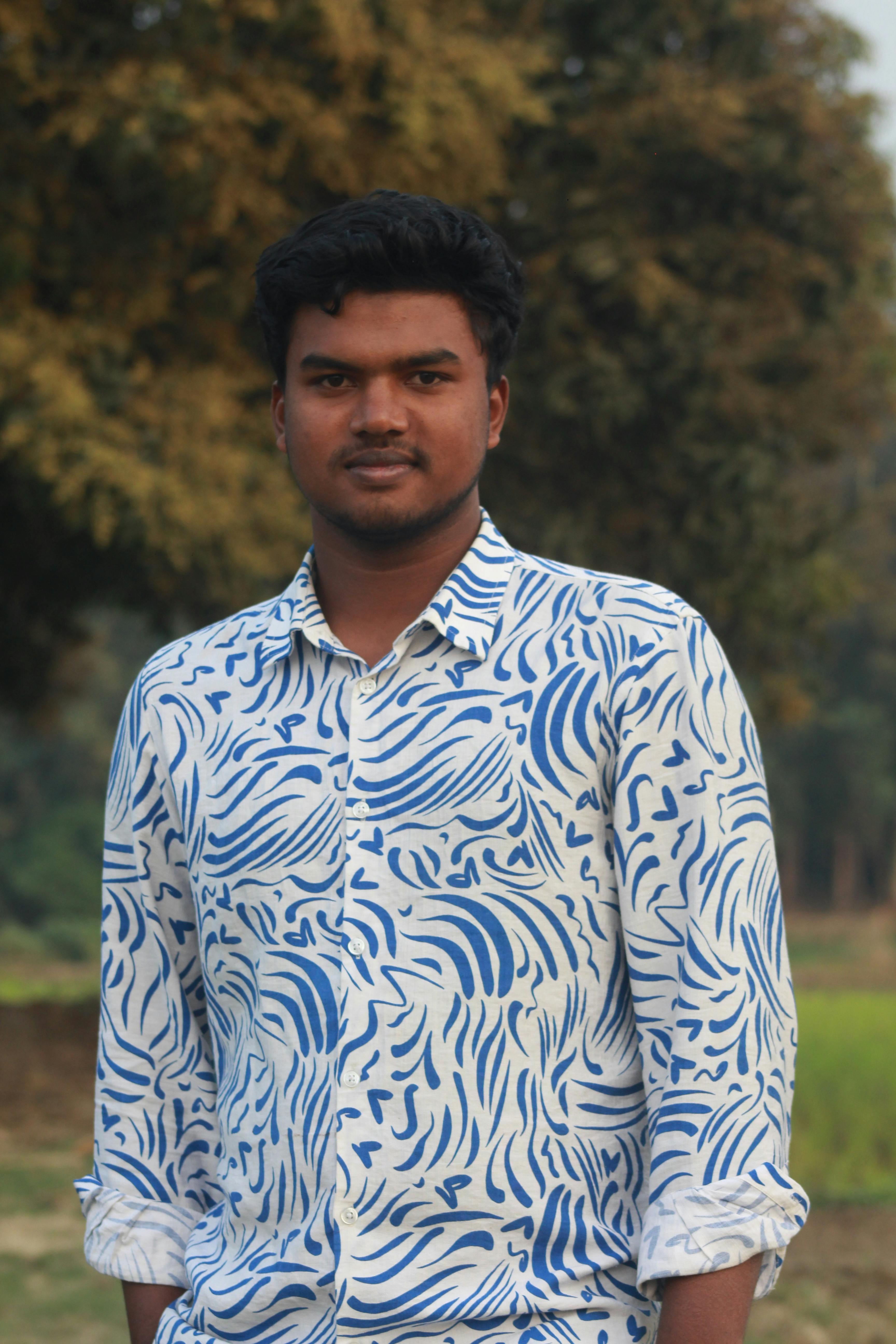 Young man standing outdoors with trees and field in the background.