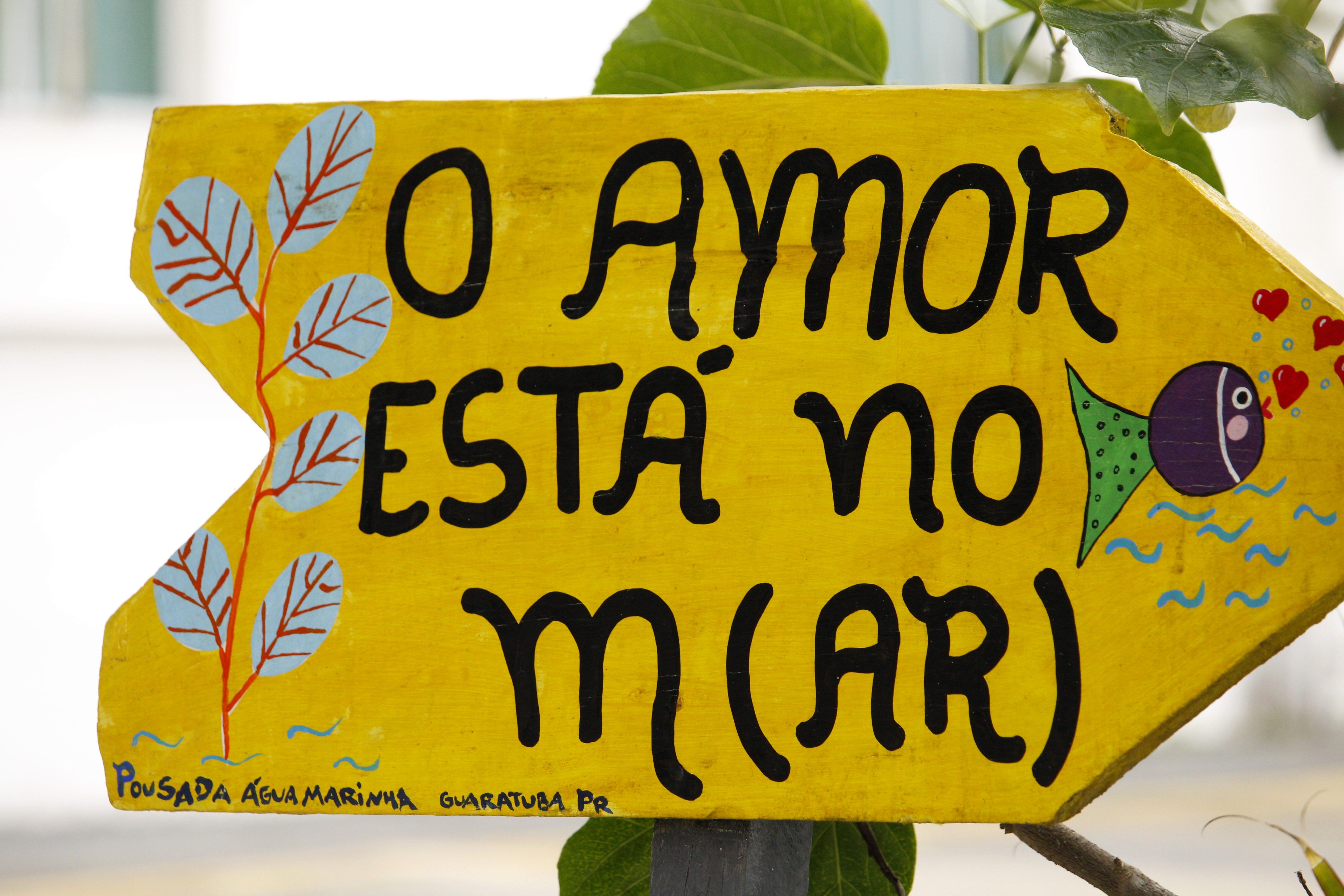 Bright yellow sign in Guaratuba with phrase 'O Amor Está no Mar,' highlighting love and sea theme.