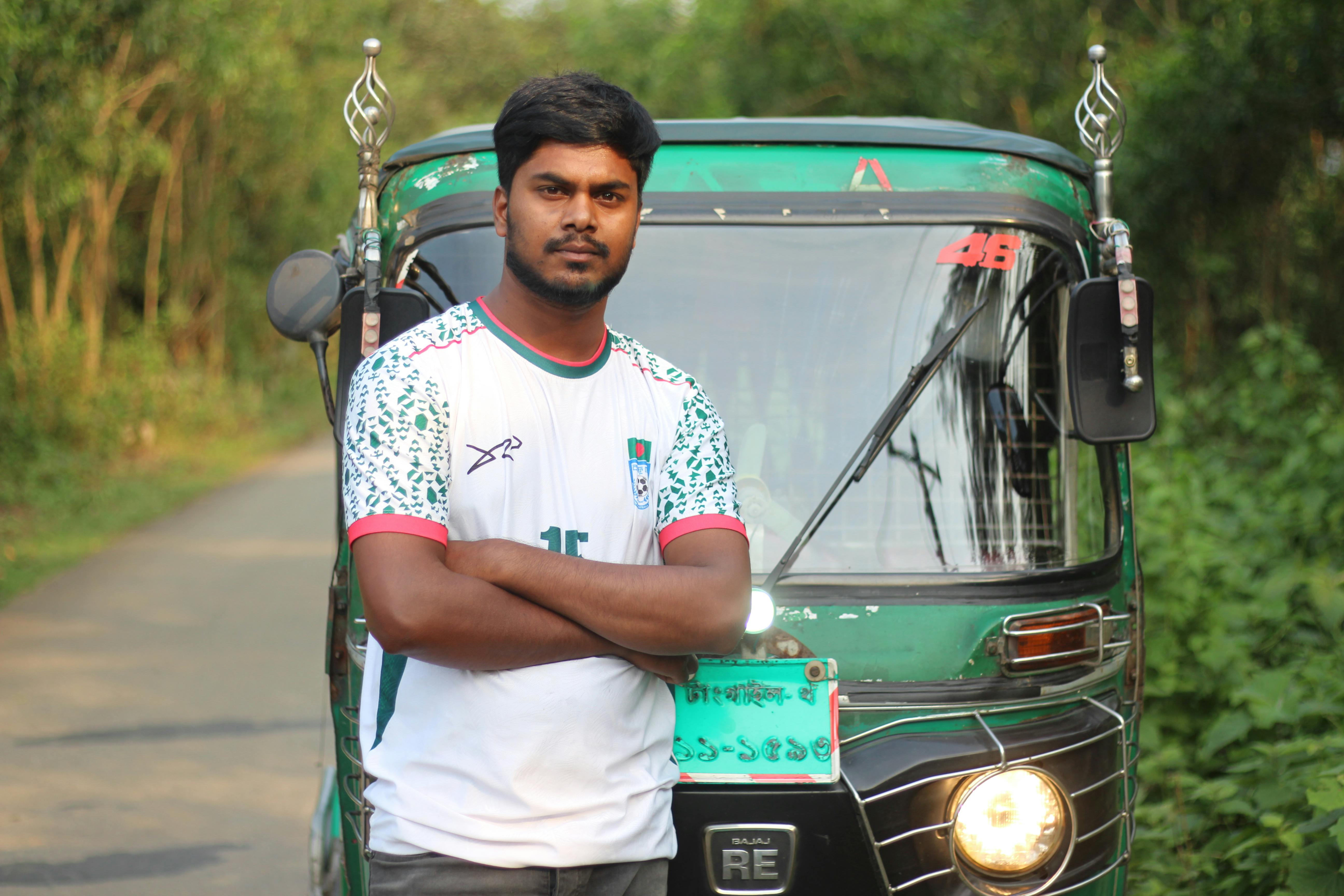 Man standing confidently in front of a green rickshaw on a peaceful rural road.