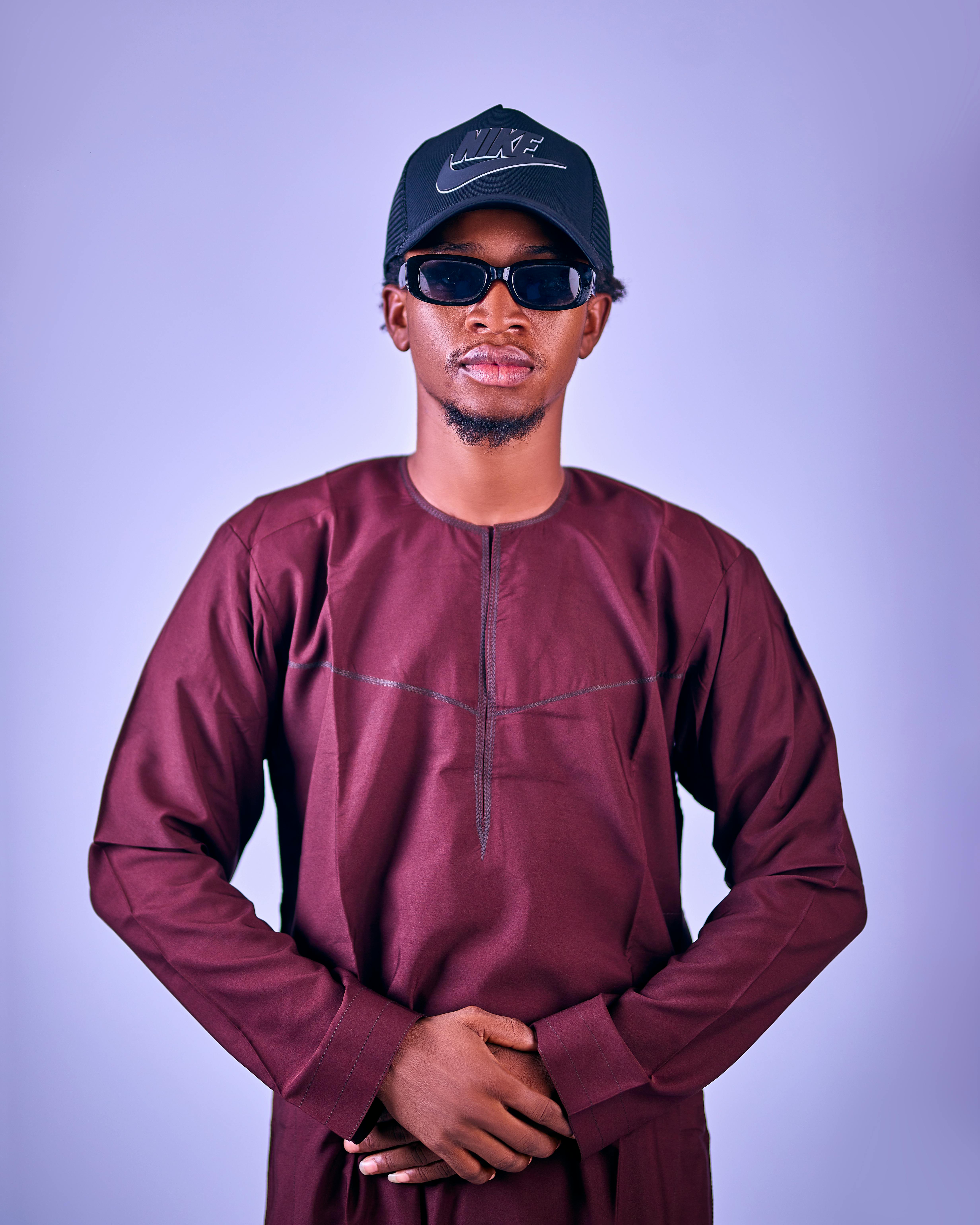 Portrait of a fashionable African man in traditional agbada attire with sunglasses and a cap.