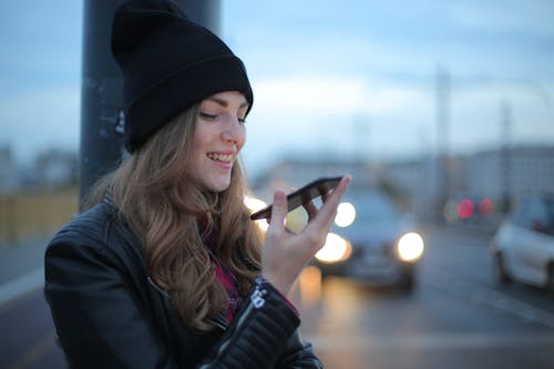 Woman in Black Knit Cap and Black Jacket Holding Smartphone