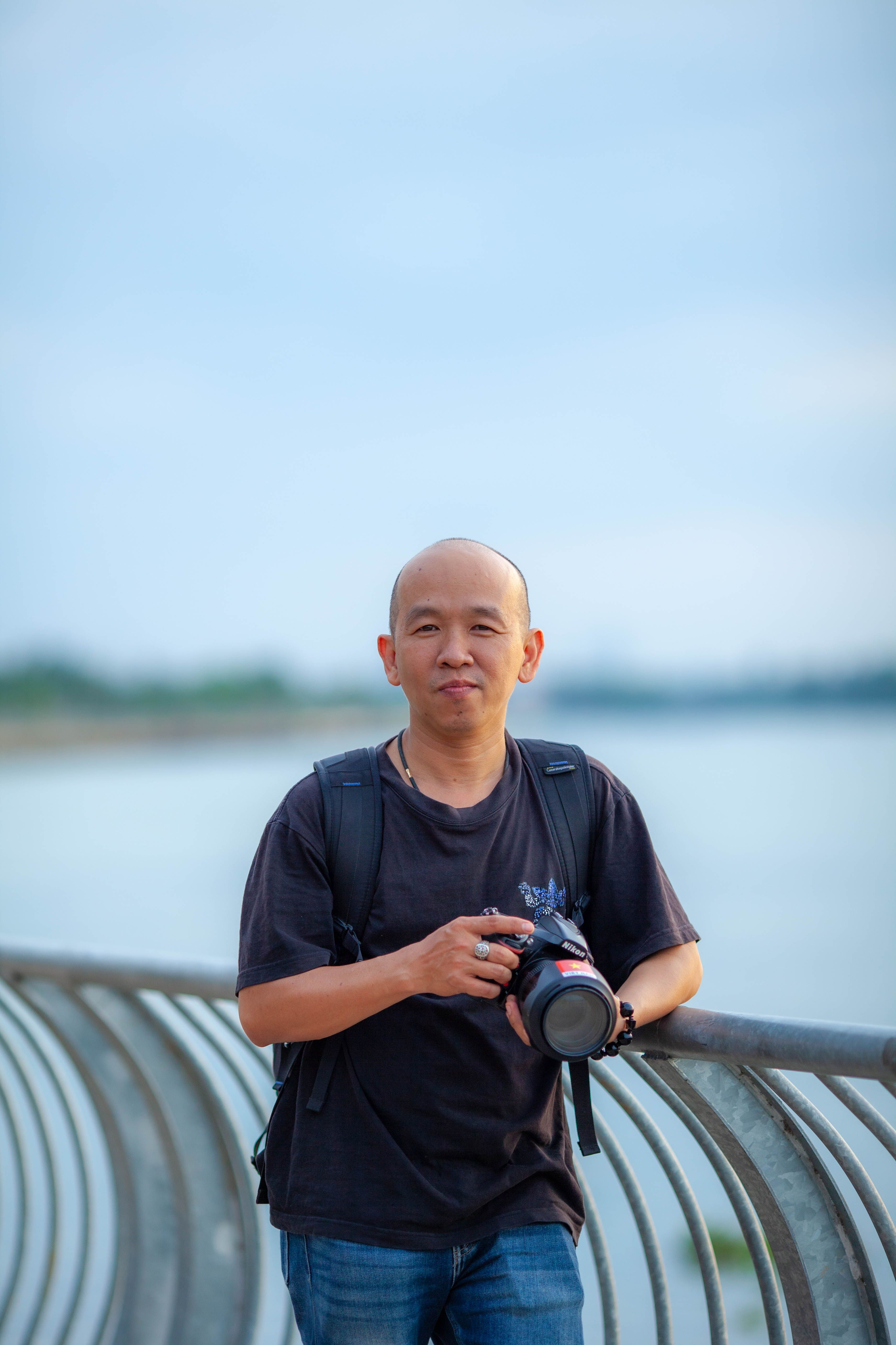 Casual portrait of a photographer holding a camera by the waterfront.
