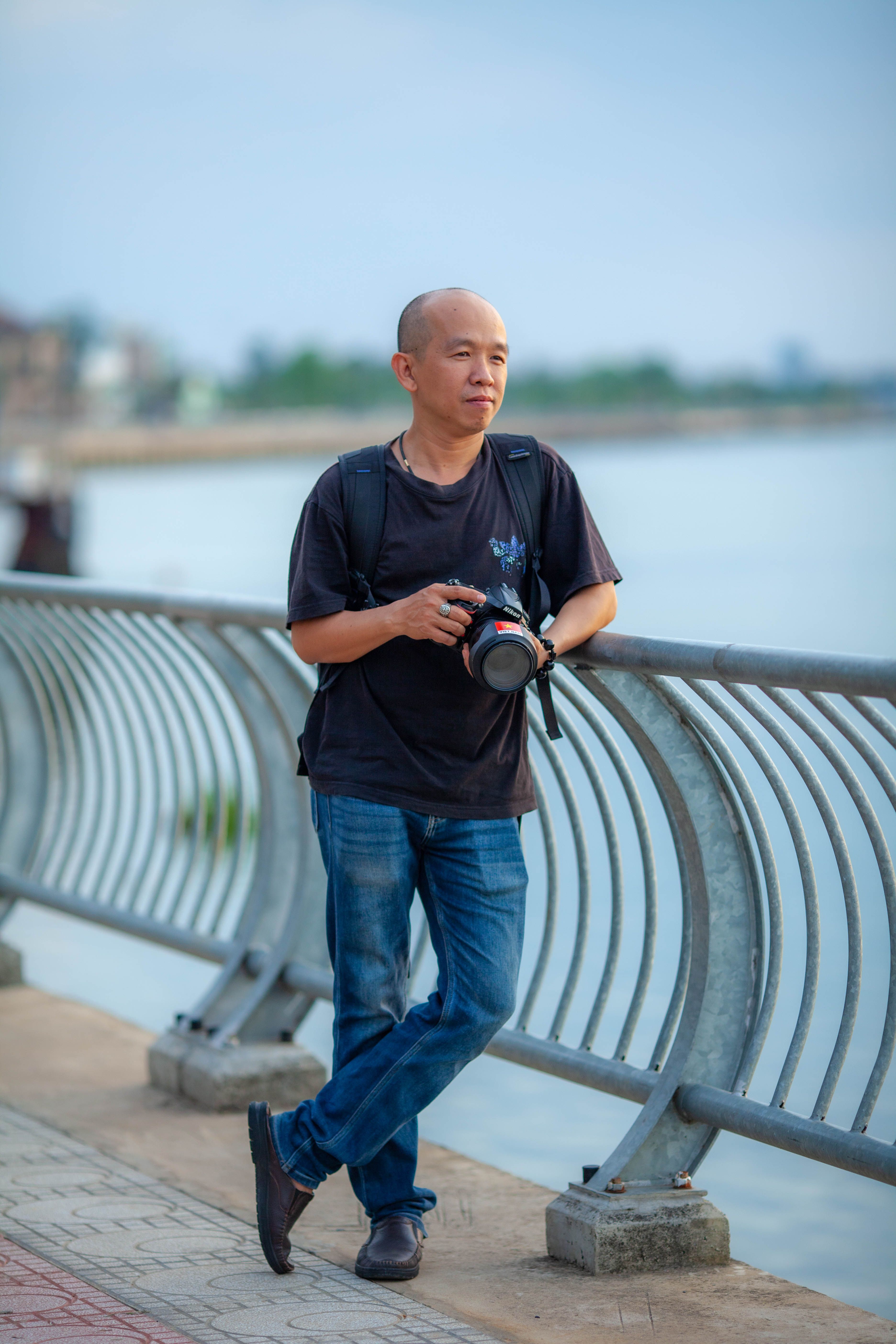 Portrait of a photographer leaning against railings by a tranquil riverfront.