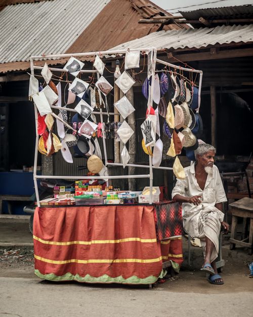 Free Elderly man selling caps and jewelry on a street-side stall in a rural setting. Stock Photo