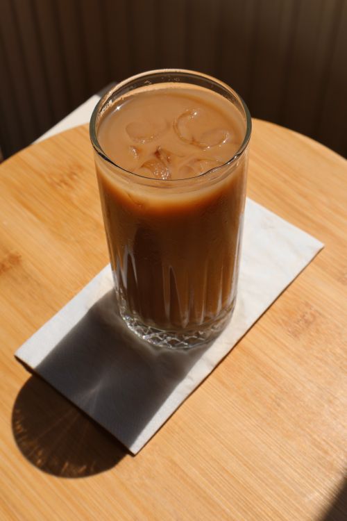 Free A glass of iced coffee on a wooden table, bathed in natural sunlight. Stock Photo