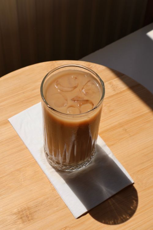 Free A glass of creamy iced coffee with ice cubes on a wooden tabletop in natural light. Stock Photo