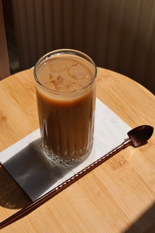 Free Glass of iced coffee on a wooden table with warm sunlight casting shadows. Stock Photo