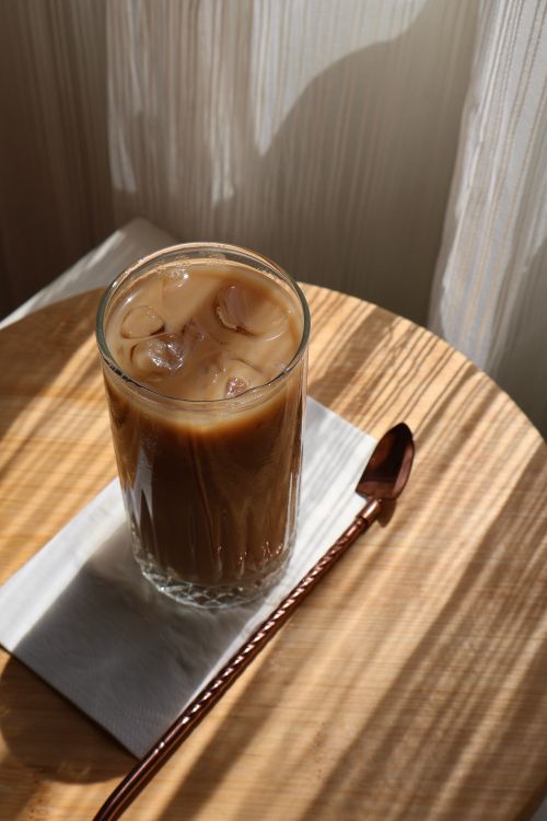 Free A tall glass of iced coffee on a wooden table bathed in natural sunlight. Stock Photo