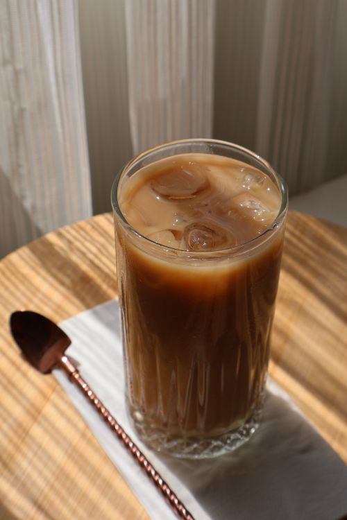 Free Glass of iced coffee on a table with spoon in warm sunlight. Stock Photo