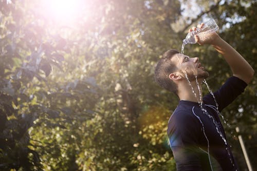 Мужчина в синей футболке с круглым вырезом поливает лицо водой