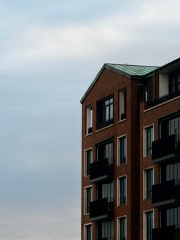A contemporary brick apartment building with balconies under a cloudy sky.