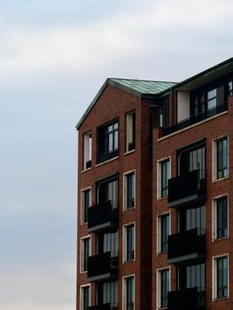 A contemporary brick apartment building with balconies against a cloudy sky.