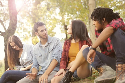 From below of diverse young people in casual clothes sitting on grass and talking