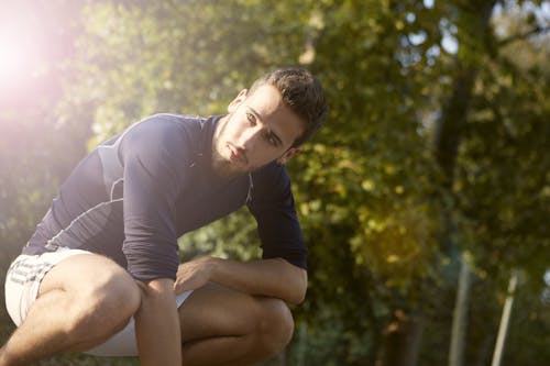 Concentrated sportsman in activewear crouching in park while resting during fitness training and looking away