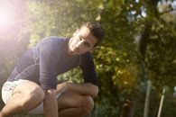 Concentrated sportsman in activewear crouching in park while resting during fitness training and looking away