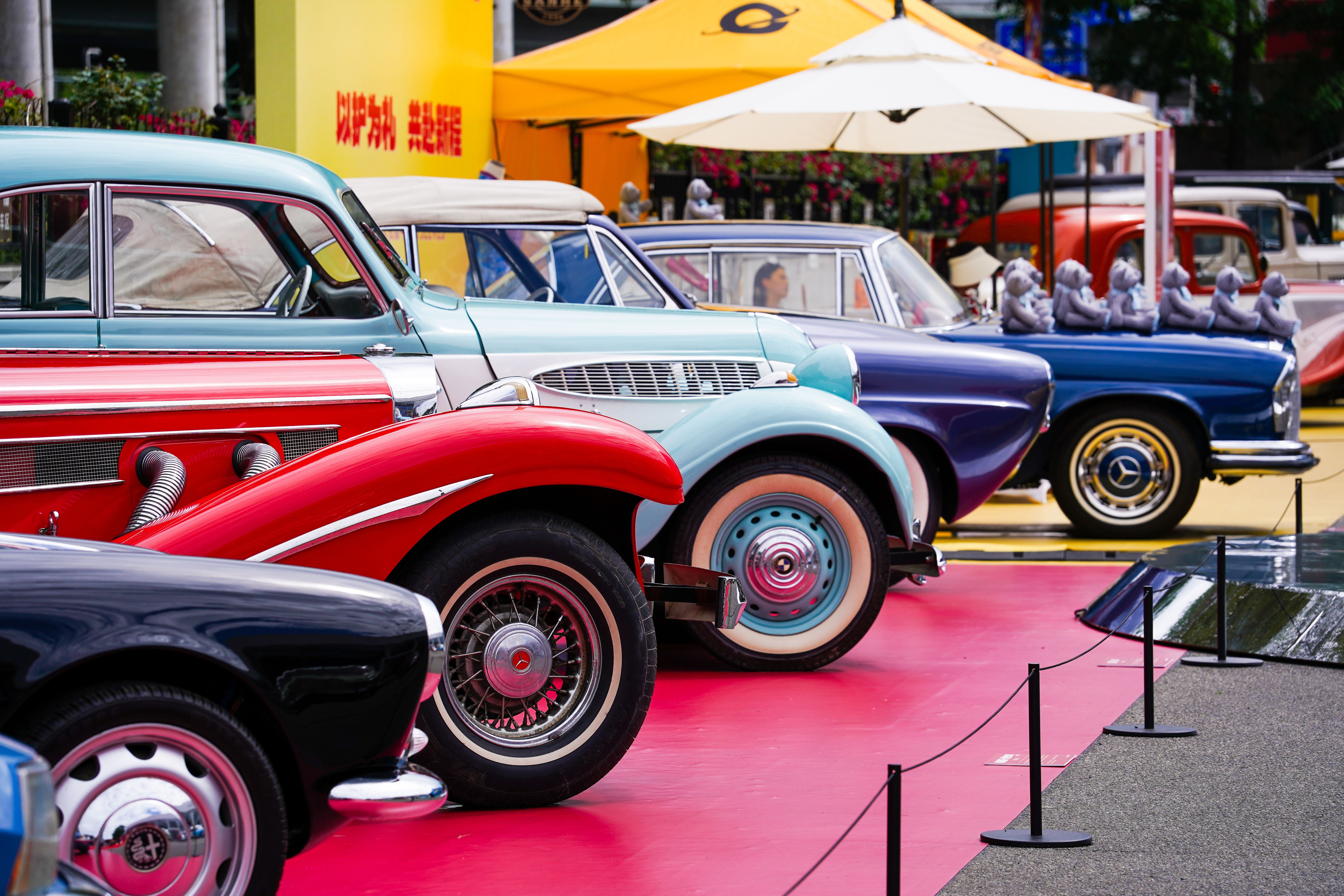 A row of colorful vintage cars showcased at an outdoor auto exhibition.