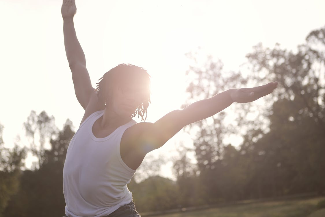 Free Sportsman in undershirt raising arms while doing exercises in sunny day in park Stock Photo