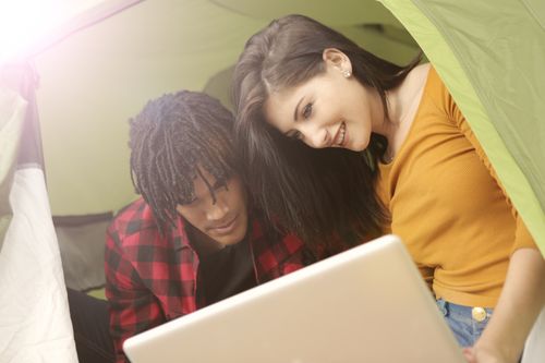 Free A young couple enjoying a laptop while camping in a tent during a sunny day. Stock Photo