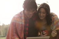 一对夫妇裹着毯子，在户外面带微笑地享受咖啡