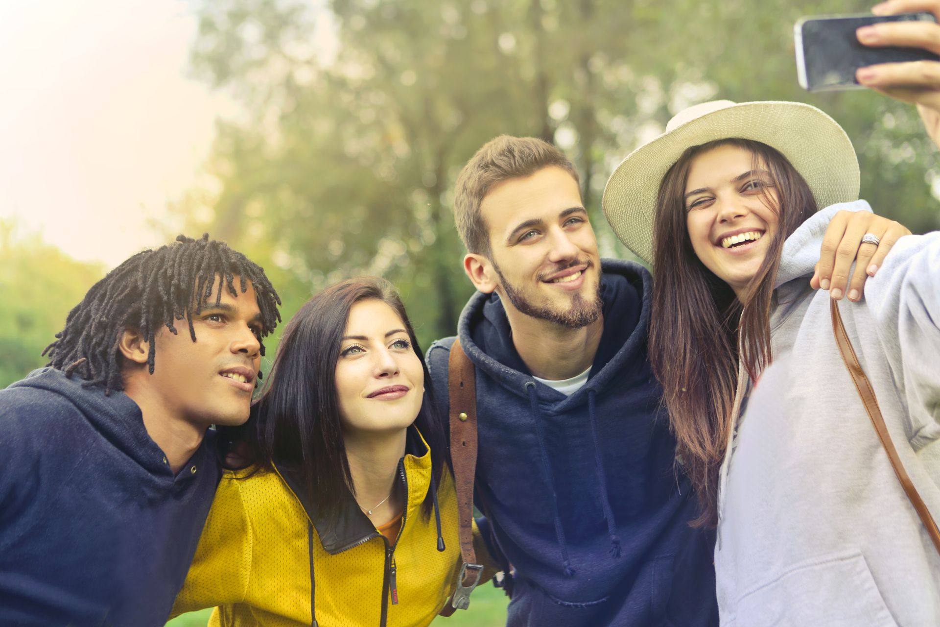 Young friends smiling and taking a selfie in a sunny park setting.