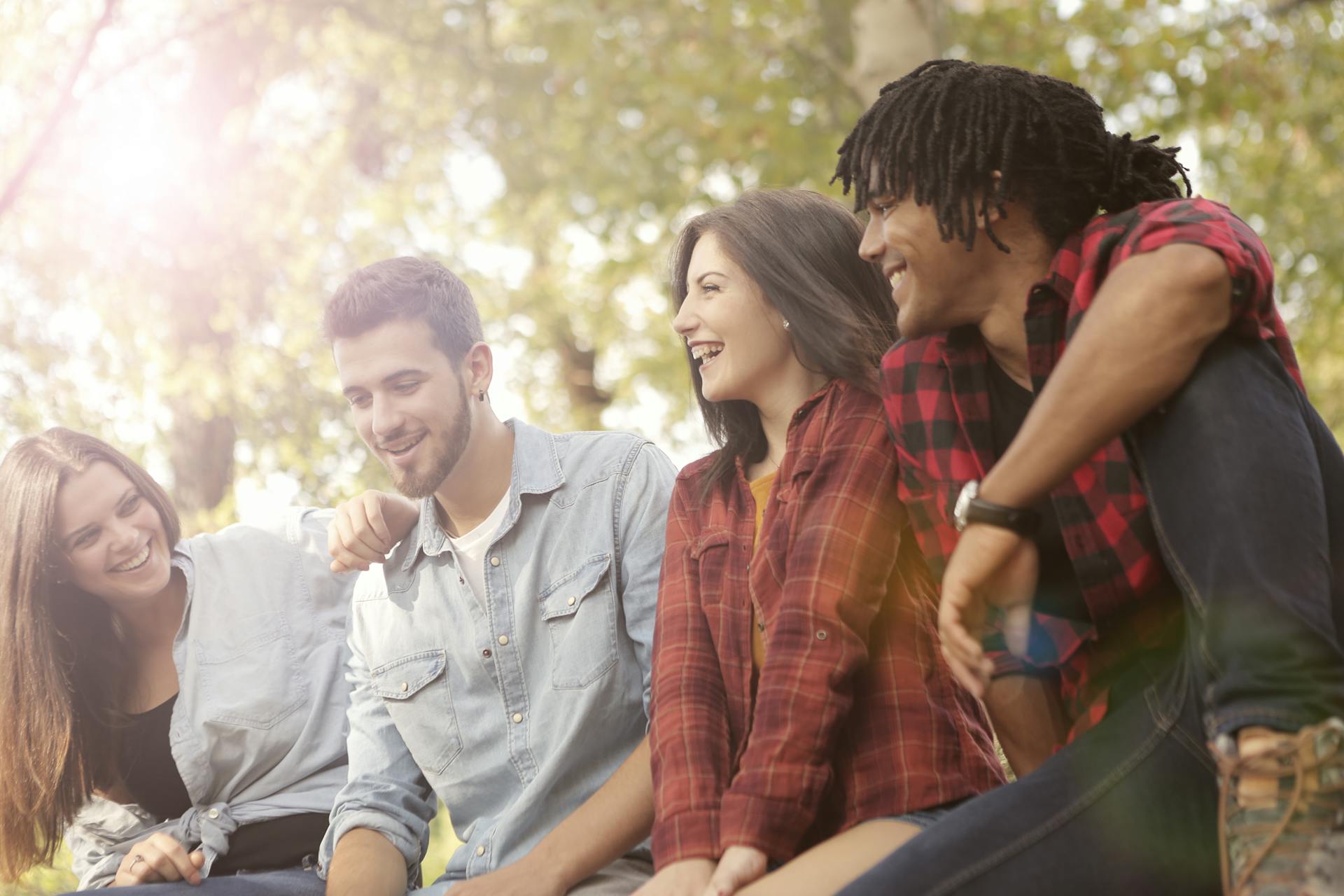 A joyful group of friends laughing in nature with sunlight filtering through the trees.