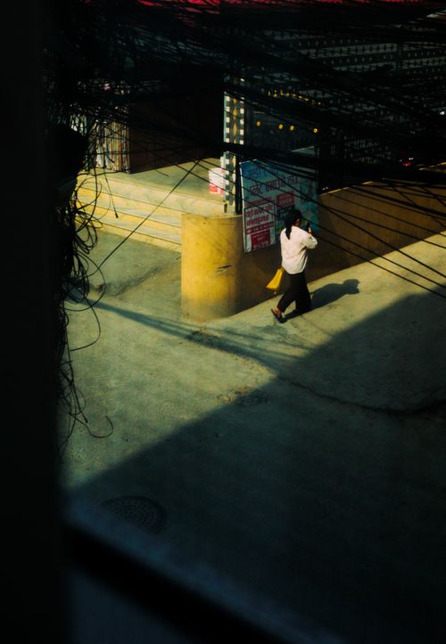 Free A lone pedestrian walks under intricate overhead wires casting shadows on a sunlit street. Stock Photo
