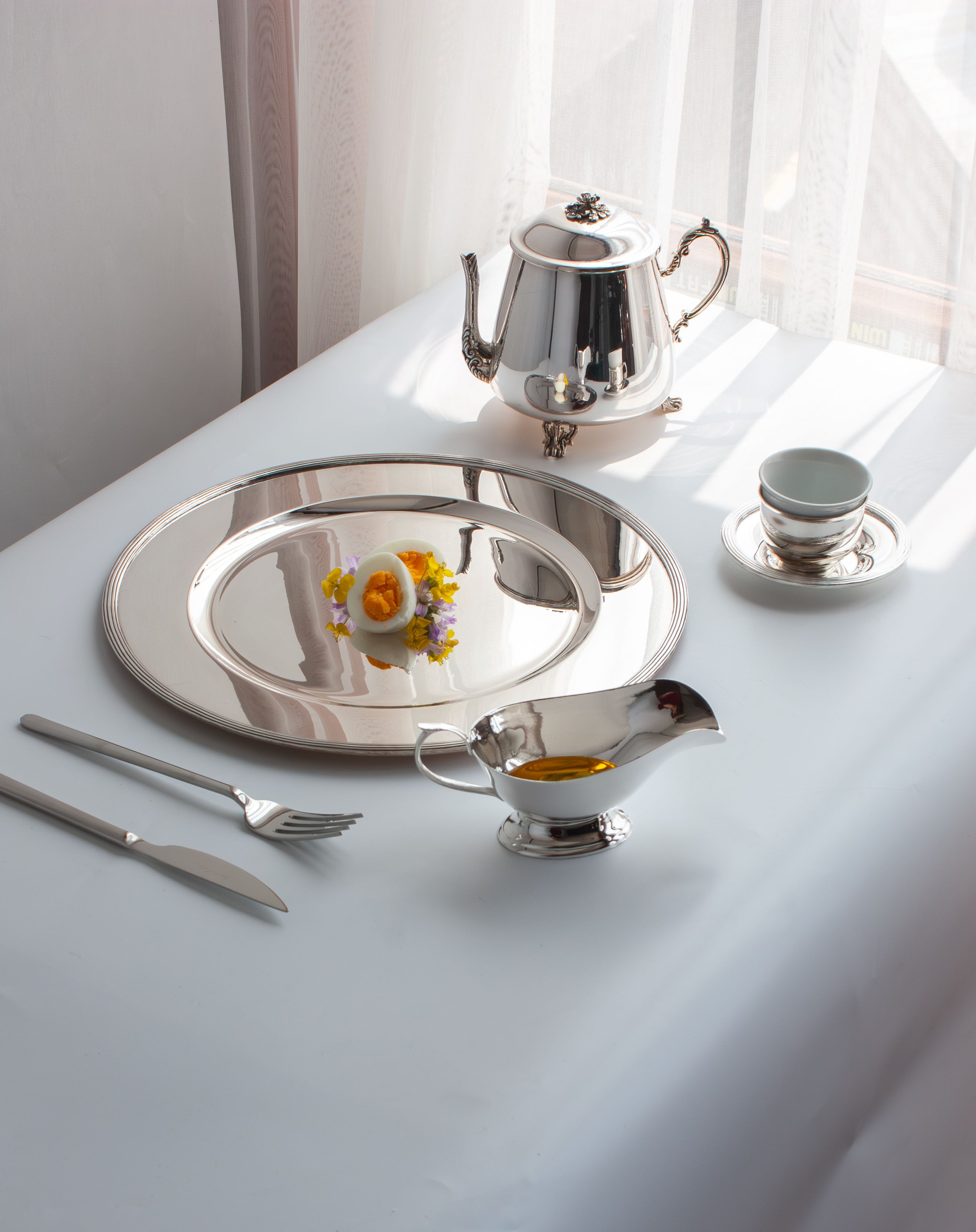 Stylish setup of a silver tea set with elegant tableware and decorative flowers, ideal for luxury dining concepts.