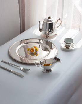 Stylish setup of a silver tea set with elegant tableware and decorative flowers, ideal for luxury dining concepts.