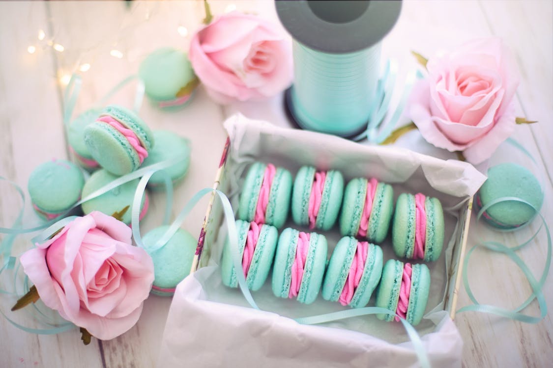 Box of mint and pink macarons with coordinating ribbons and roses, creating a delicate and inviting presentation.
