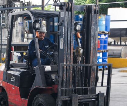 Warehouse scene with worker operating a forklift among blue barrels.