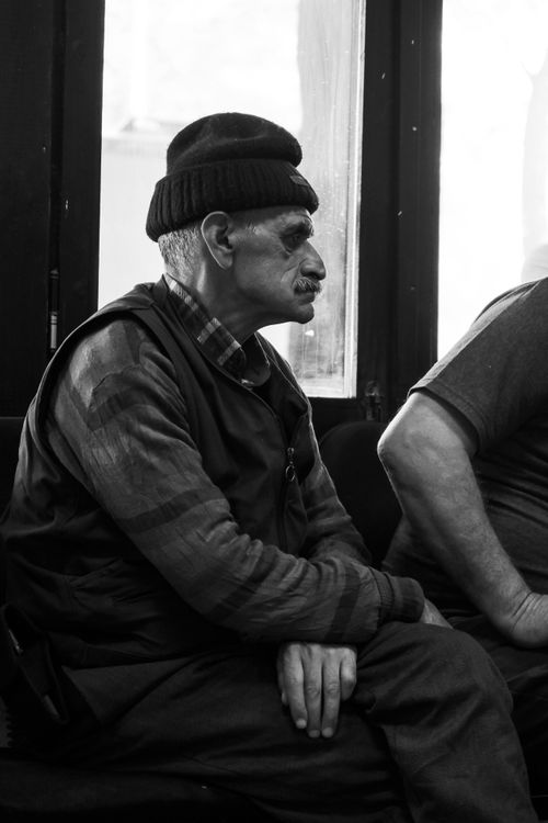 Free Black and white portrait of an elderly man in a beanie sitting thoughtfully indoors. Stock Photo