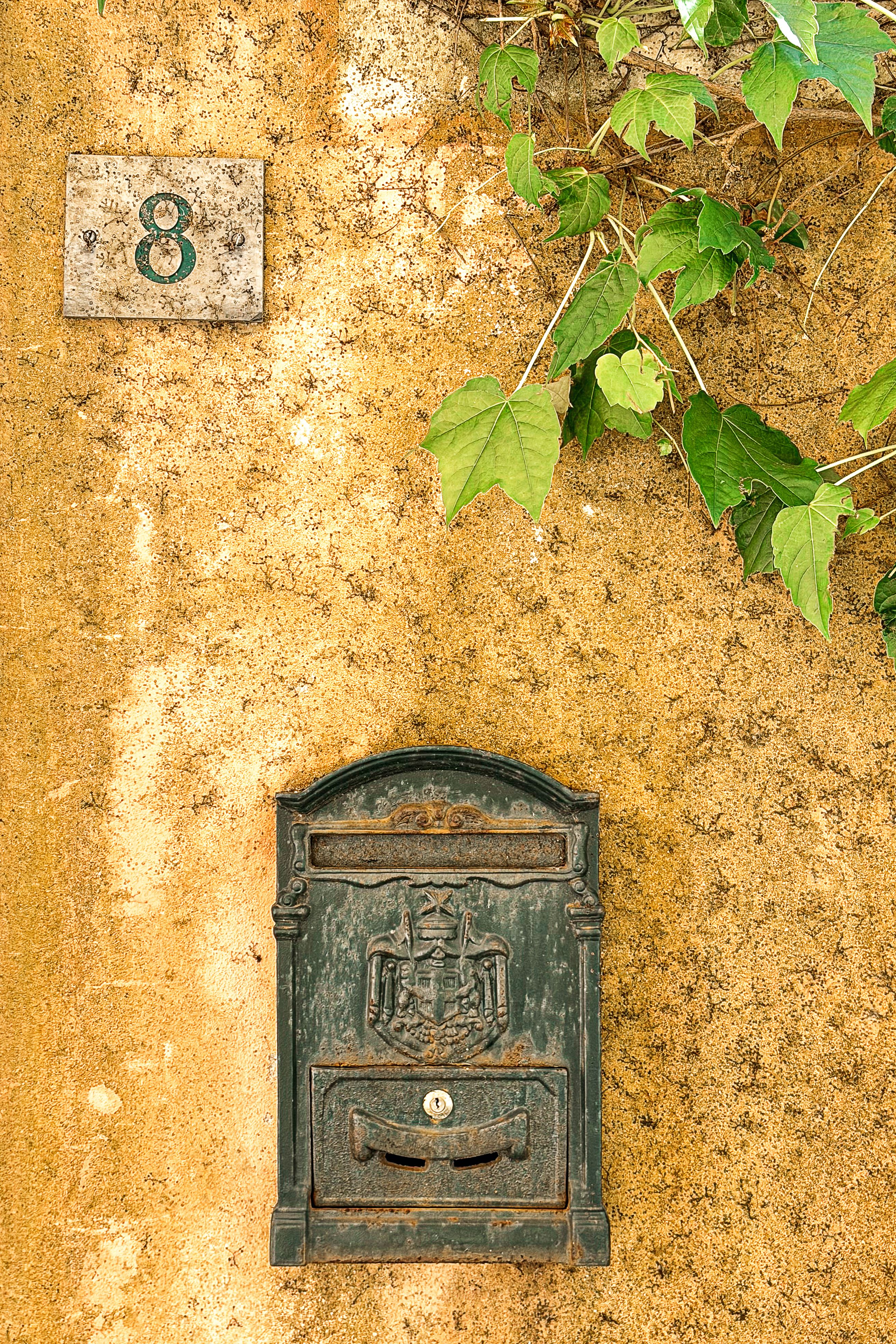 A classic Italian mailbox set against a rustic wall with ivy and number 8.