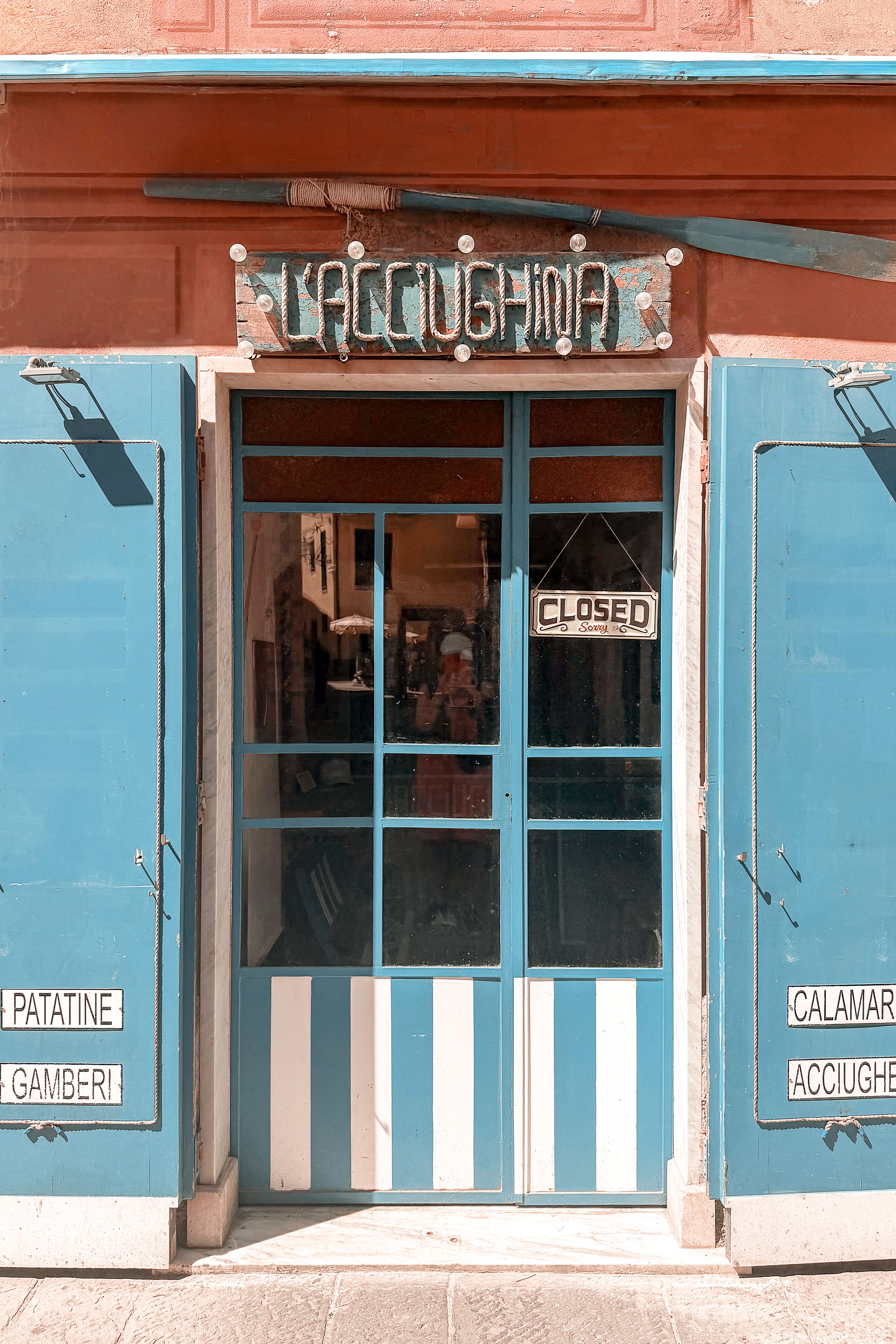 Charming closed shop entrance with blue doors and Italian signage on a sunny street.