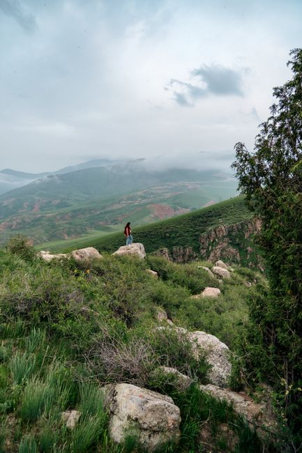 Person in lush mountainous landscape of Kyrgyzstan, amidst mist and clouds.