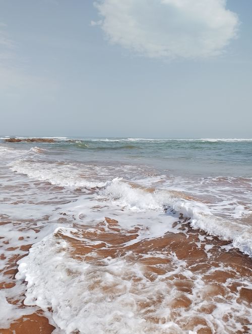 Free Peaceful ocean waves with foam rolling onto a sandy shore under a clear sky. Stock Photo