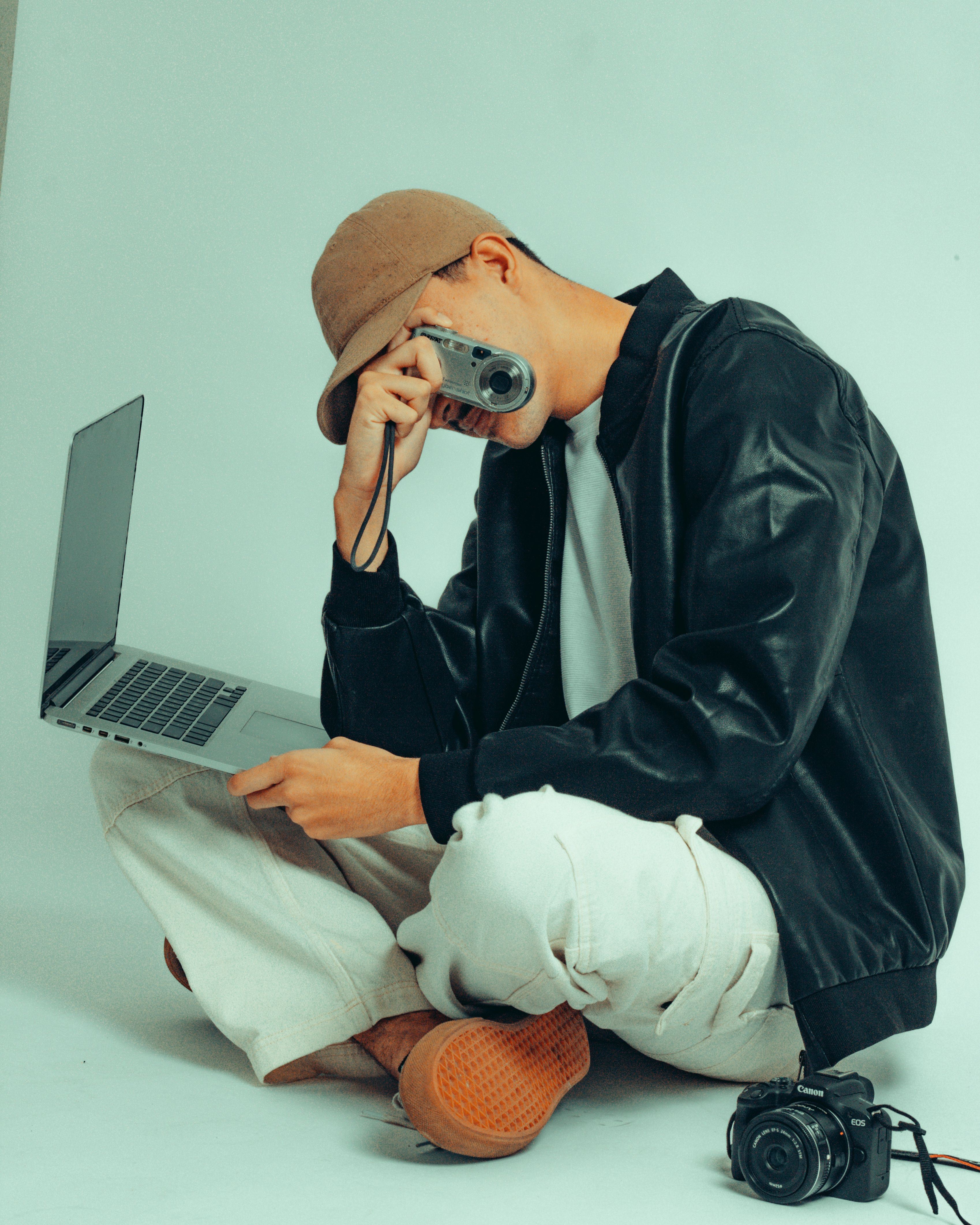 Young male photographer using a camera and laptop in a studio setting, showcasing creativity.