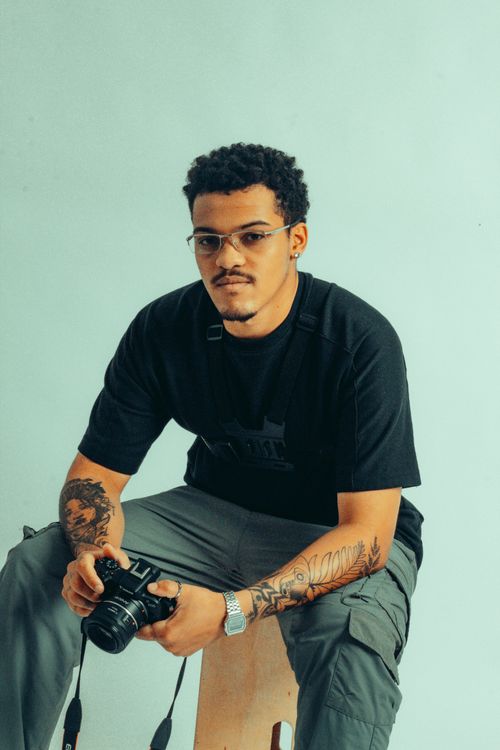 Free Portrait of a young tattooed male photographer holding a camera, sitting in a studio setting. Stock Photo