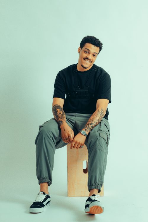Free Young man with tattoos sitting casually on a stool in a studio setting, exuding style and confidence. Stock Photo